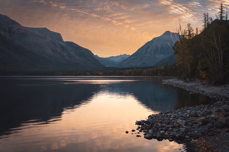 A mountain lake in Glacier National Park reflecting a warm clouded sky