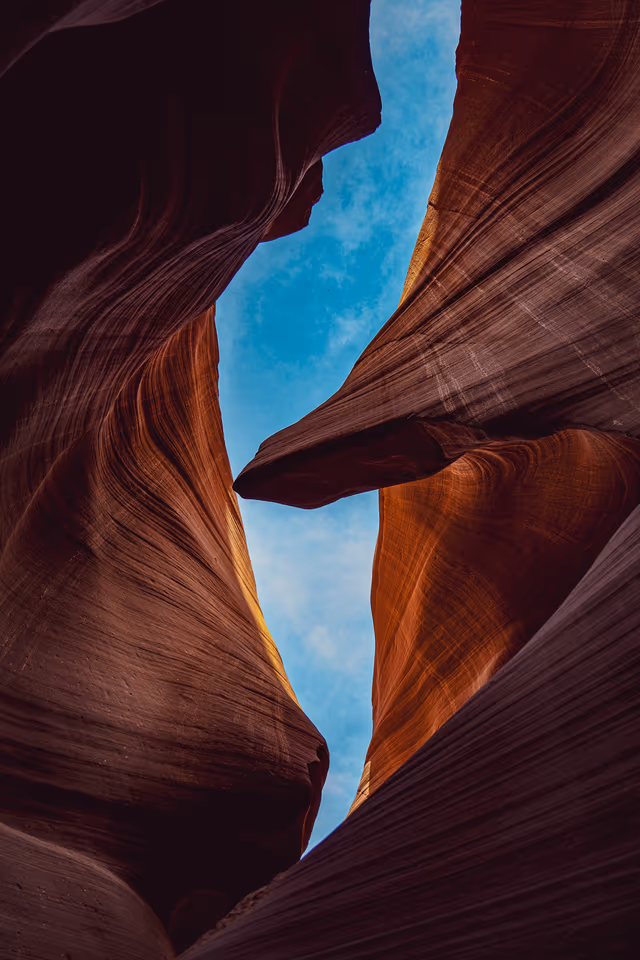 Curving red sandstone walls opening to blue sky in Antelope Canyon