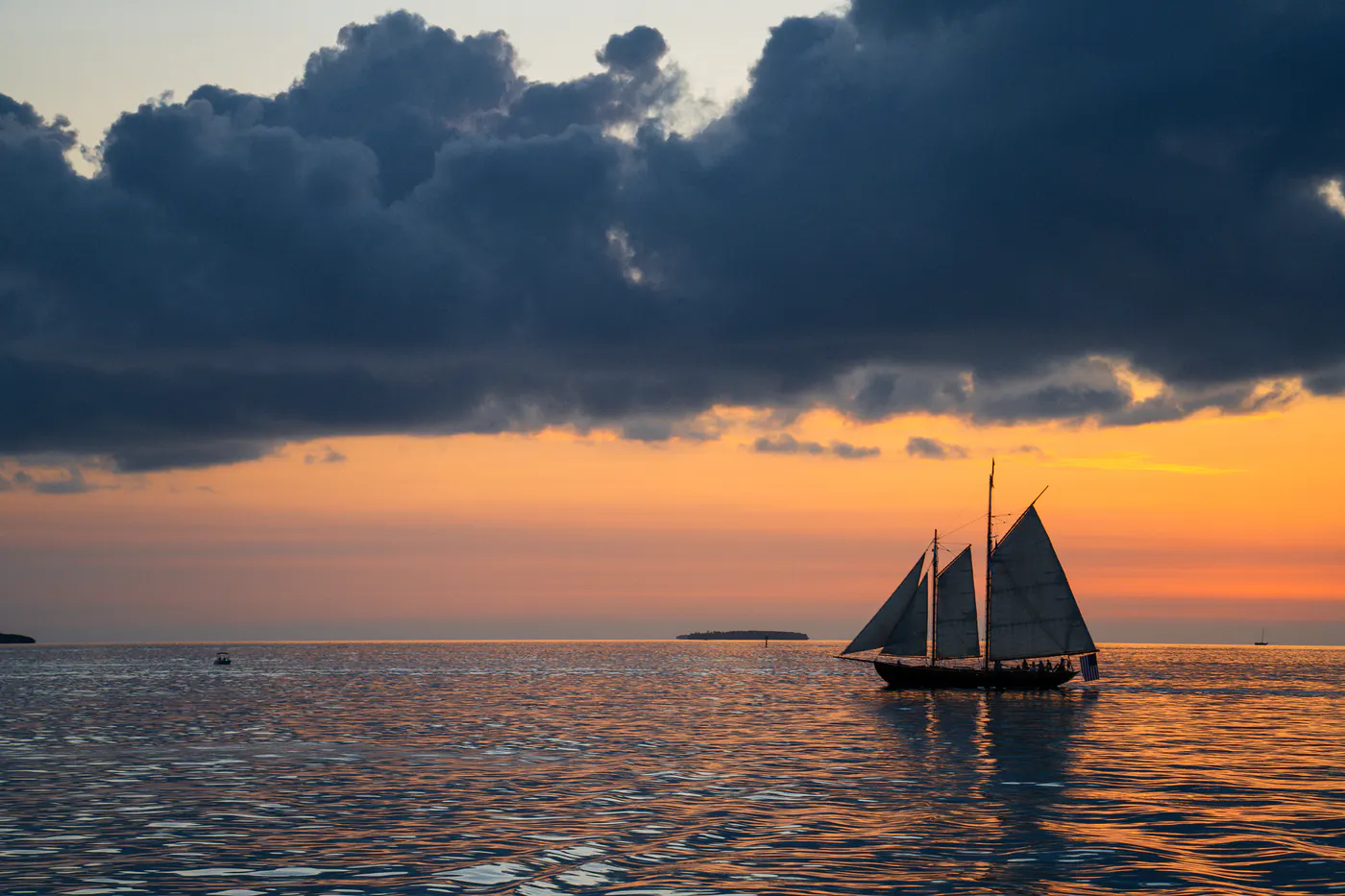 A silhouetted sailboat crossing calm water beneath storm clouds at sunset