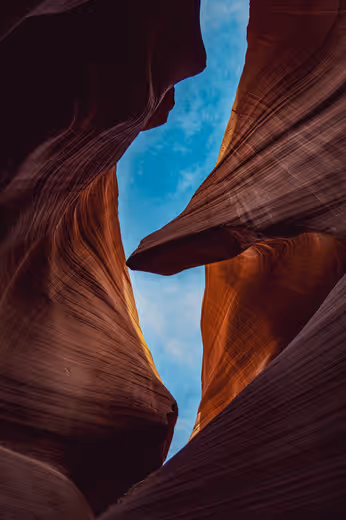 Curving red sandstone walls opening to blue sky in Antelope Canyon