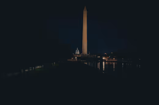 The Washington Monument illuminated at blue hour with a dark reflecting pool
